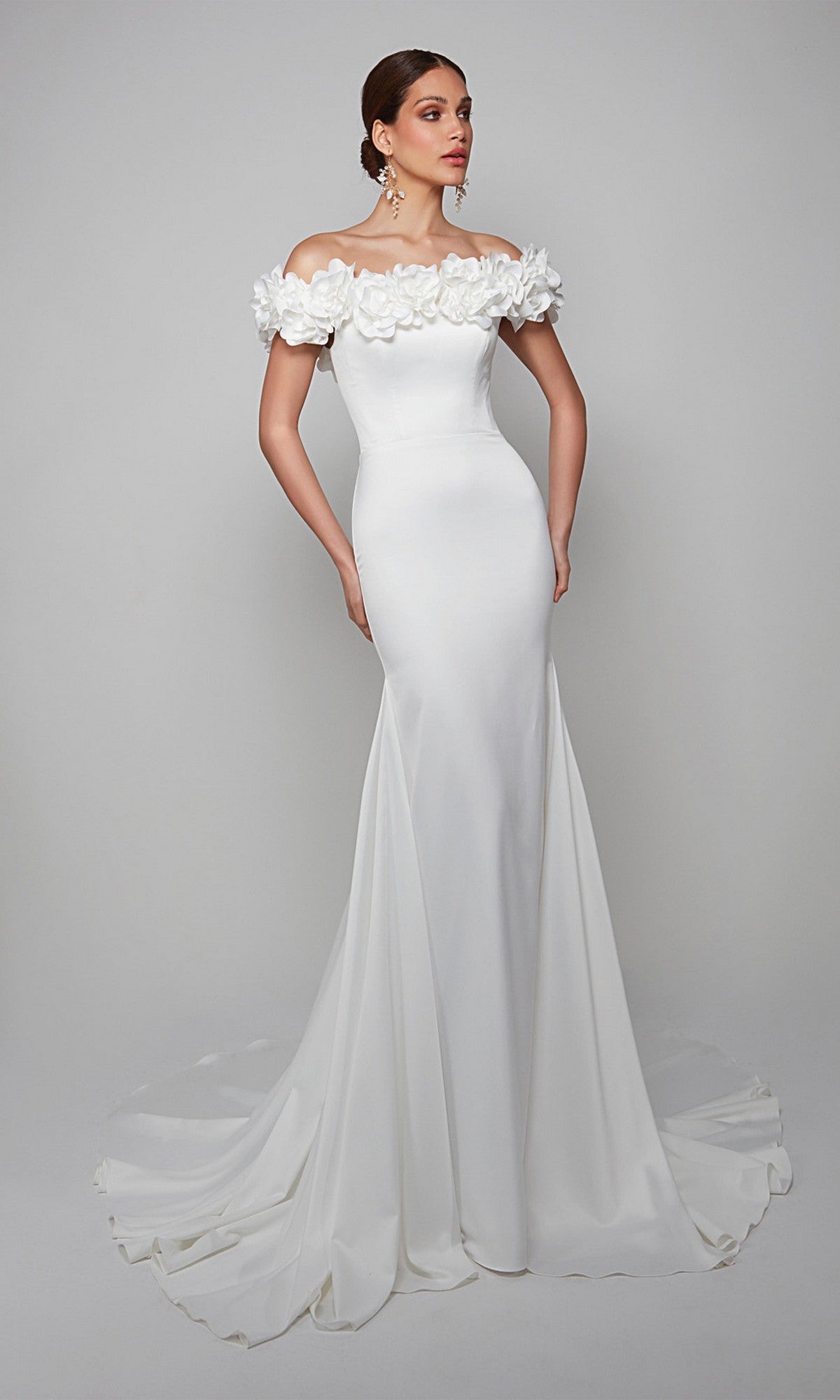 A woman wears the Alyce 7061 long formal dress in diamond white, featuring an off-the-shoulder neckline with floral details and a flowing train for timeless elegance.
